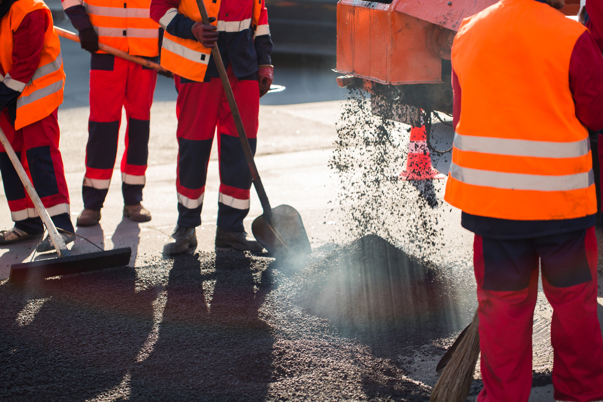 Road construction crew spreading hot asphalt during a street resurfacing project using paving equipment and hand tools.